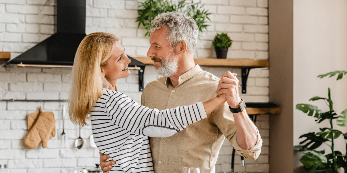 Middle age man and woman dancing in a kitchen and smiling